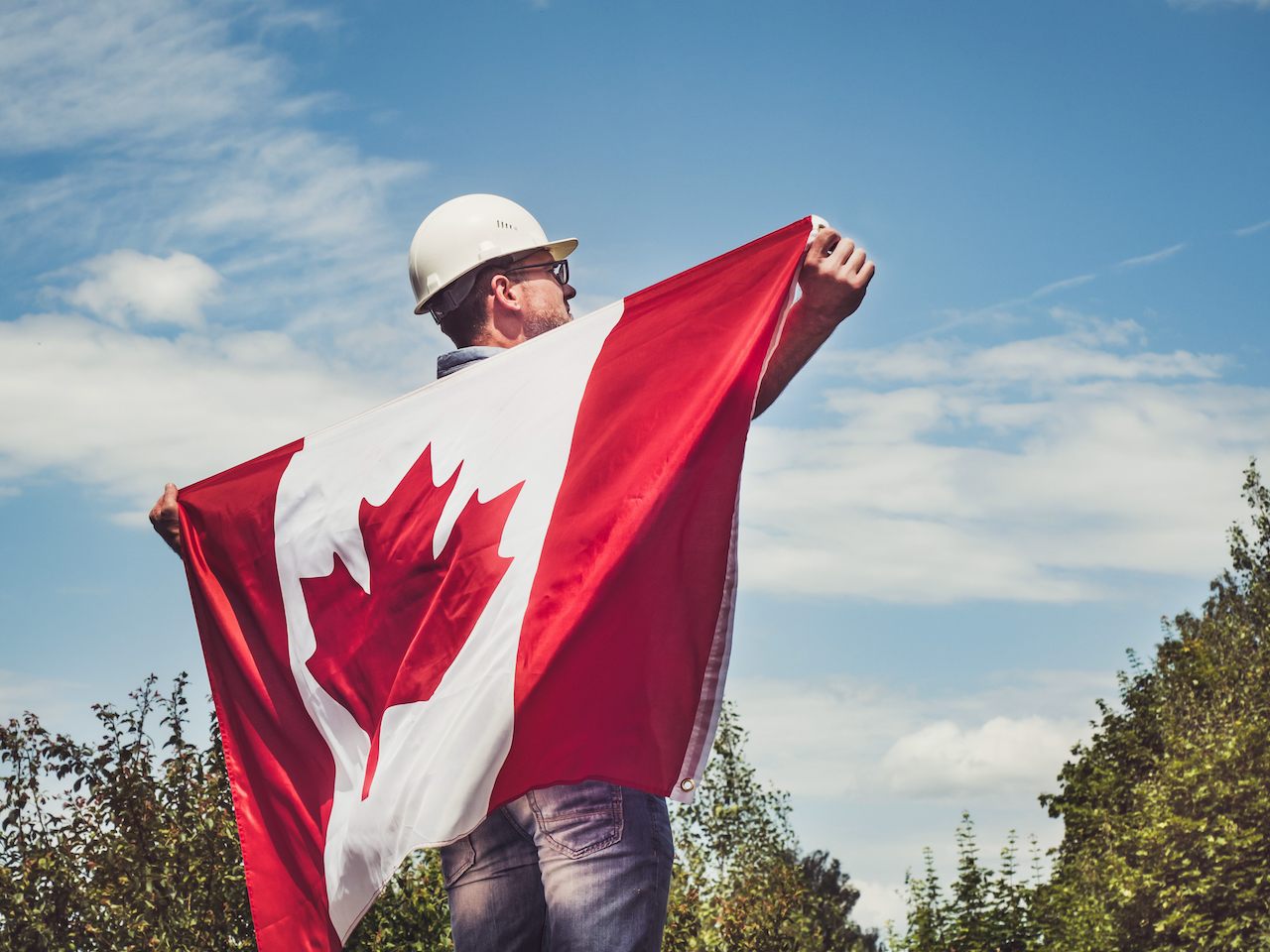 A worker in a hard hat holding a Canadian flag